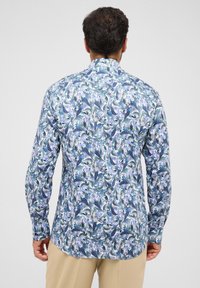 Camicia a maniche lunghe con motivo floreale blu e foglie verdi, texture liscia, dettagli a bottoni sui polsini e orlo curvo sul retro.