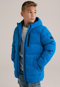 Chaqueta puffer azul con capucha, que presenta un cierre frontal, bolsillos laterales y un parche de logo negro en la manga, hecha de material liso e insulated.
