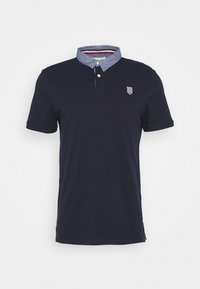 Marinblå kortärmad polo med en chambray-krage och en liten broderad logo på bröstet. Tillverkad av ett mjukt, strukturerat tyg.