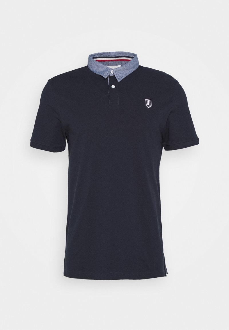 Marinblå kortärmad polo med en chambray-krage och en liten broderad logo på bröstet. Tillverkad av ett mjukt, strukturerat tyg.