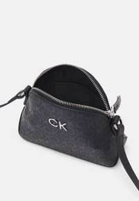 Borsa a tracolla nera in sintetico con chiusura a zip, caratterizzata da un motivo sottile e un accento in logo metallico, texture liscia e tracolla regolabile.