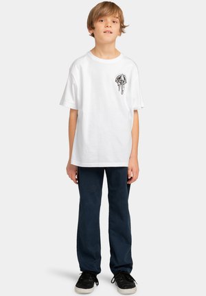 T-shirt bianco a maniche corte con design grafico nero sul lato sinistro del petto, abbinato a pantaloni blu navy e scarpe nere.