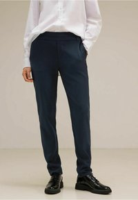 Navy tailored trousers with a smooth texture, slim fit design, and a solid pattern. Worn with a white shirt and black lace-up shoes.