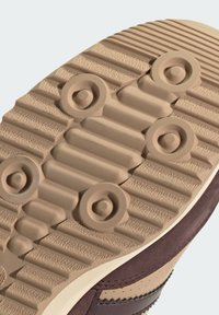 Semelle de chaussure en caoutchouc beige texturé, présentant des accents circulaires et des rainures pour une meilleure adhérence, avec des détails en daim et en cuir marron sur le côté.