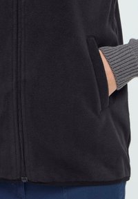 Schwarze Fleecejacke mit Reißverschluss, ausgestattet mit Seiten Taschen und gerippten grauen Bündchen, die sichtbar sind. Weicher Stoff und einfaches Design.