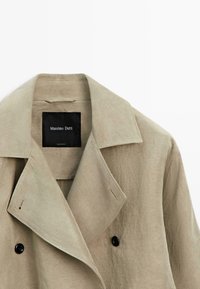 Beige dobbeltradet frakke med brede revers, sorte knapper og et sort "Massimo Dutti" mærke inden i kraven.