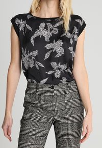 Black short-sleeve blouse with white floral pattern, paired with high-waisted black and white checked trousers, featuring a tailored design.