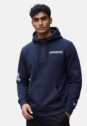 Uomo che indossa una felpa con cappuccio Cowboys blu navy con tasca frontale, mezza zip, coulisse e toppa con logo sulla manica sinistra.
