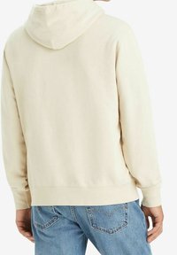Felpa color crema con cappuccio regolabile. Realizzata in tessuto morbido, presenta polsini e orlo a costine. Indossata con jeans in denim blu.