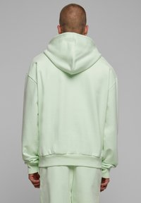 Sudadera de color verde claro con una capucha grande, corte relajado y puños y dobladillo acanalados. Textura suave y lisa sin patrones ni acentos visibles.