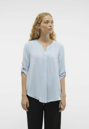 Blusa azzurra chiara a maniche lunghe con scollo a V, in tessuto texturizzato, maniche arrotolate e orlo curvo, abbinata a pantaloni neri.