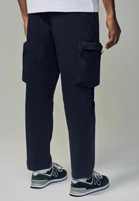 Pantalones cargo azul marino con dos bolsillos laterales, detalles de cremallera, diseño de pierna recta, material de mezcla de algodón, combinados con zapatillas deportivas negras.