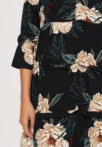 Vestido negro con estampado floral que presenta grandes peonías en tonos beige y verde, mangas acampanadas, diseño en capas y una cintura ajustada con detalles de cordón.