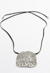 Pendentif en métal argenté avec un design de coquillage texturé sur un cordon en ruban noir ; forme ronde, motif détaillé et surface lisse et réfléchissante.