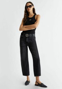 Top negro sin mangas con un logo, jeans de mezclilla negra de cintura alta y mules negras de punta con detalle de hebilla; diseño elegante y contemporáneo.