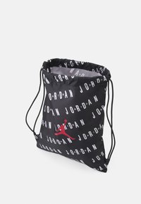 Crna torba s vezicom od izdržljive tkanine, s bijelim tekstom "JORDAN" rasprostranjenim po cijeloj površini i crvenim Jumpman logom.