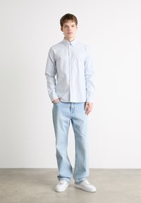 Chemise boutonnée à rayures bleu clair, à manches longues, associée à un jean en denim bleu clair et des baskets blanches. Design minimaliste avec un ajustement simple.