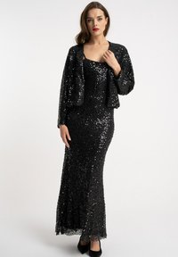 Czarna wieczorowa suknia z cekinami o dopasowanym kroju, połączona z krótką kurtką z cekinów. Suknia ma delikatne rozszerzenie na dole.