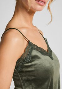 Olivengrünes Satin-Cami mit Spitzenbesatz entlang des Ausschnitts und verstellbaren Trägern, ausgestattet mit einer weichen, glatten Textur.