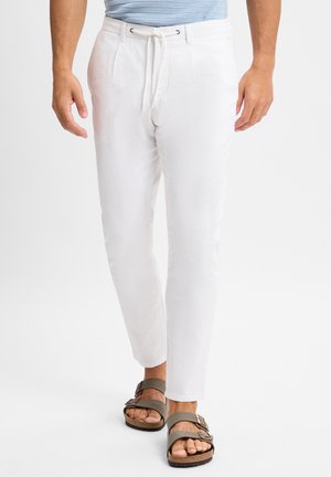 Witte linnen broek met een taps toelopende pasvorm, een elastische tailleband en een trekkoordsluiting. Gepaard met bruine sandalen met banden.