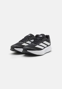 Une paire de chaussures de course athlétiques noires et blanches avec un dessus en mesh et de épaisses semelles blanches sur un fond clair.