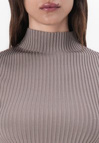 Ribbade polotröja i dämpad taupe. Har en figursydd design med hög krage och en slät, elastisk textur.