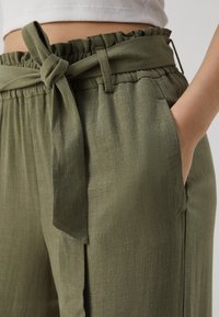 Pantalon vert olive en tissu doux et texturé, doté d'une taille froncée et d'une ceinture nouée. Comprend des poches latérales et une coupe décontractée.