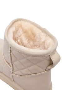 Botín beige hasta el tobillo con diseño acolchado, forro suave y esponjoso en beige, material exterior texturizado y una lengüeta para facilitar el calzado.