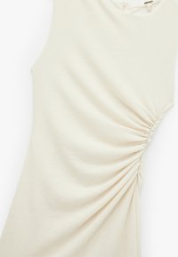 Robe de couleur crème avec un tissu texturé, présentant un détail froncé sur le côté et un col rond, adaptée pour un usage décontracté.