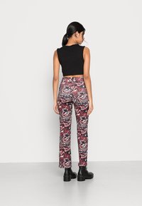 Top cropped preto combinado com calças justas de padrão colorido apresentando redemoinhos de vermelho, branco e preto. Botas pretas grossas.