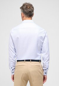 Camicia a maniche lunghe di colore azzurro chiaro con motivo, con dettagli di bottoni scuri ai polsini, abbinata a pantaloni beige. Design del colletto semplice.