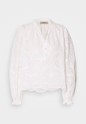 Blouse blanche avec un motif découpé complexe, fermeture à boutons sur le devant, encolure ronde et poignets élastiqués. Tissu doux, coupe ample, ourlet festonné.