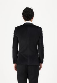 Blazer negru din catifea cu o textură netedă, cu o decupare simplă și mansete butonate, asociat cu pantaloni negri, văzut din spate.