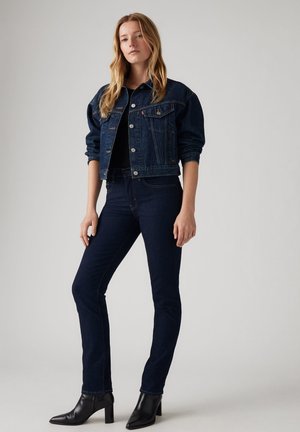 Donkerblauwe denim jacket met een cropped ontwerp, knoopsluiting en klassieke zakken. Strakke donkerblauwe jeans, gecombineerd met zwarte enkellaarsjes met hak.