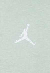 Tessuto verde chiaro con una morbida texture, caratterizzato da un logo Jumpman ricamato in bianco, raffigurante una posa in volo che cattura il movimento e l'atleticità.