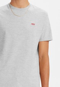 T-shirt gris à manches courtes en coton, avec un petit logo rouge Levi's sur la poitrine et un col rond. Design minimaliste.