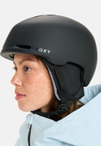 Zwarte Roxy sk helmet met matte afwerking, ventilatiegaten en gewatteerde oorkappen. Verstelbare kinband en strak ontwerp zonder graphics.