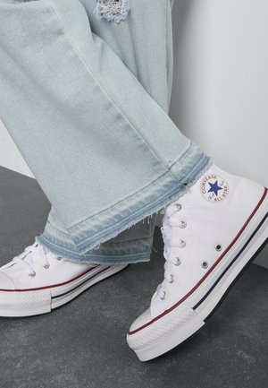 Witte canvas hoge sneakers met rode en marineblauwe accenten, gedragen met lichtblauwe spijkerbroeken met rafelige zoom en versleten plekken.