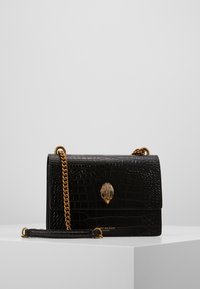 Černá kabelka z umělé krokodýlí kůže se zlatým zapínáním ve tvaru mušle, řetízkovým popruhem a strukturovaným povrchem. Kompaktní obdélníkový tvar.
