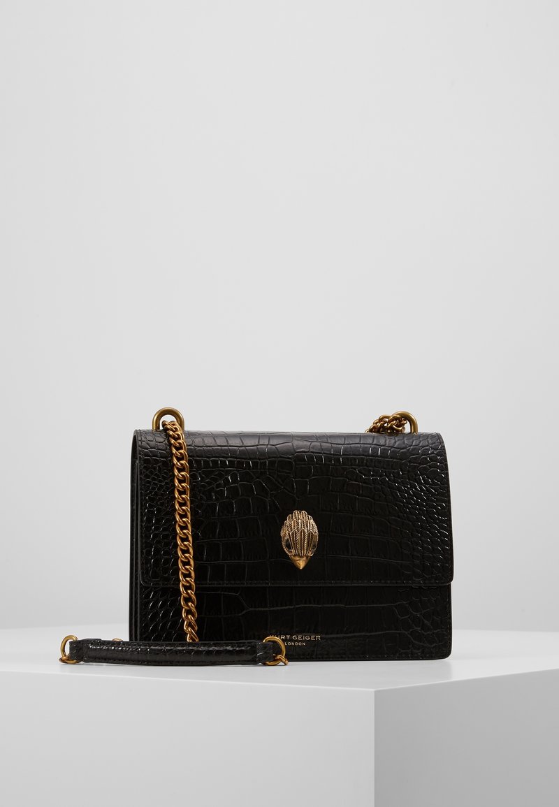 Černá kabelka z umělé krokodýlí kůže se zlatým zapínáním ve tvaru mušle, řetízkovým popruhem a strukturovaným povrchem. Kompaktní obdélníkový tvar.