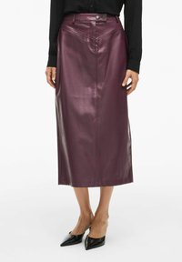 Lila Leder-Midi-Rock mit glatter Textur, vorderer Nahtdetails und zwei Knopfverschlüssen an der Taille. Getragen mit schwarzen spitzen Schuhen.