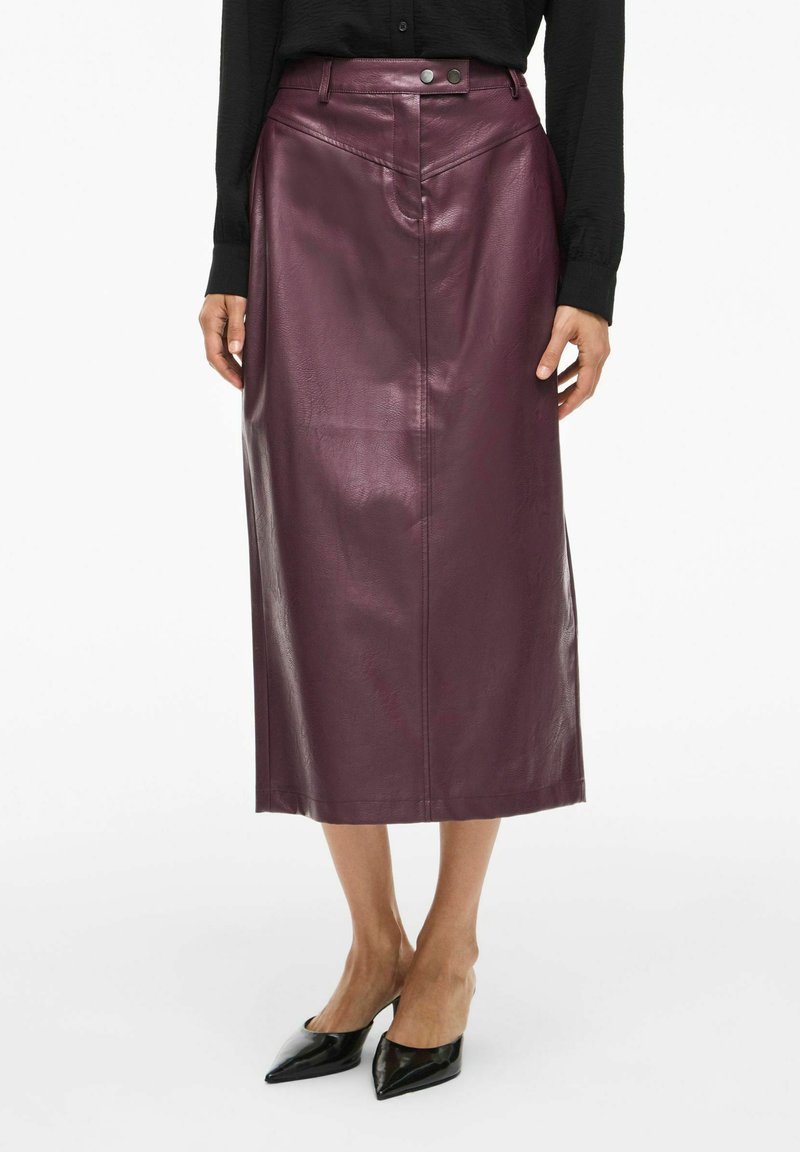 Jupe midi en cuir mauve avec une texture lisse, des détails de couture sur le devant et une fermeture à deux boutons à la taille. Portée avec des chaussures noires à bout pointu.