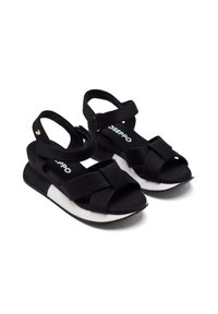 Sandalias negras con diseño de tiras cruzadas, hebilla ajustable en el tobillo, plantilla acolchada y detalle de entresuela blanca. Material de tela suave.