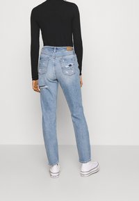 Světle modré, opotřebované džíny s viditelnými trhlinami a dvěma zadními kapsami, spojené s černým upnutým topem a bílými teniskami.