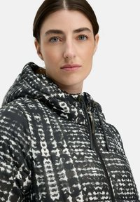 Kapuzenshirtjacke im Schwarz-Weiß-Muster, mit einem gesteppten Design, Reißverschluss und verstellbaren Kordeln an der Kapuze.