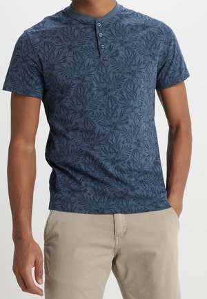 Chemise à manches courtes bleu marine avec motif floral, col Henley à trois boutons, texture de tissu douce, portée avec un pantalon beige clair.