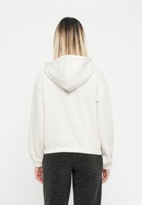 Ανοιχτό γκ ρι φούτερ με κουκούλα, σε χαλαρή εφαρμογή, με ελαστικές μανσέτες και κουκούλα με κορδόνι, συνδυασμένο με σκοτεινά παντελόνια με λεοπάρ μοτίβο.