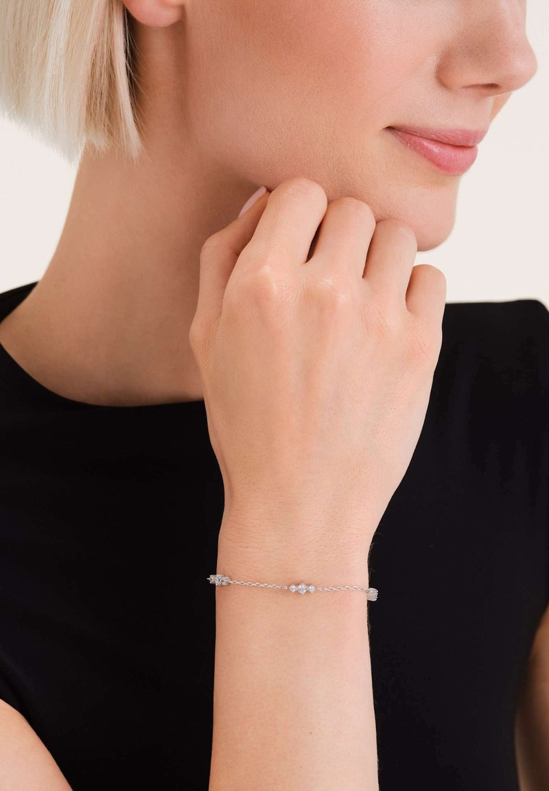 Silver bracelet featuring a delicate chain with small geometric accents. The design is minimalist with a smooth texture.