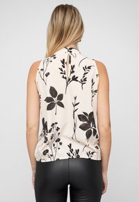 Bloemenprint mouwloze top in beige en zwart, met een hoge hals, keyhole rugdetail en een elastische onderrand.