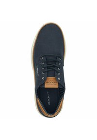 Dark navy canvas shoe with tan leather accents and white rubber sole. Features lace-up design and branded insole. Smooth textured surface.